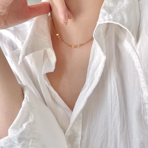 Detail of a minimalist gold disk choker necklace worn over a white cotton shirt