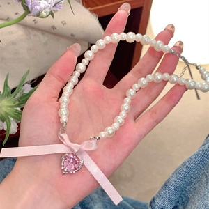 Detail of pink silk bow and heart crystal pendant on white pearl necklace