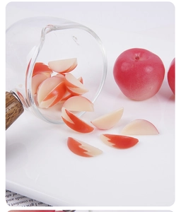 Miniature red apple slice models pouring from a glass cup onto a white table