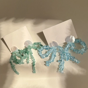 Détail de boucles d'oreilles nœuds en perles avec pierres bleues et vertes sur carte