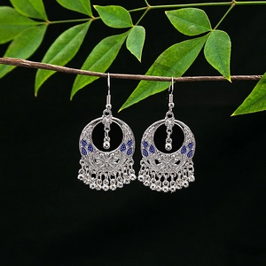 Detail of silver alloy boho earrings with blue enamel and tassel beads on a branch