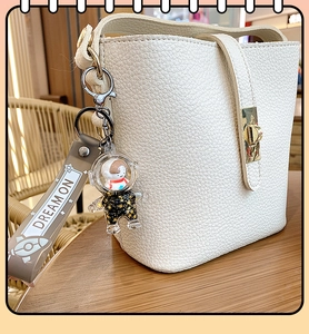 Detail of white pebbled bucket bag with astronaut liquid sand keychain and gold clasp