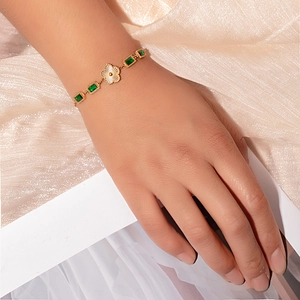 Close-up of a gold bracelet featuring emerald green square stones and a floral charm detail