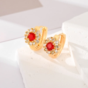 Detailed close-up of golden flower earrings with central red stone and white zircon stones