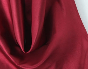 Gros plan sur un tissu satin bordeaux montrant des plis élégants et une texture soyeuse