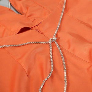 Close-up of orange satin jumpsuit featuring sparkling rhinestone chain detailing