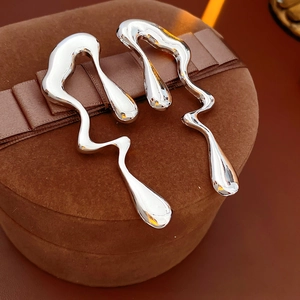 Gros plan de boucles d'oreilles argentées en forme de goutte liquide sur écrin en suède