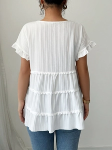 Elegant white textured short sleeve top with ruffle sleeves and tiered hem on white background