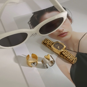 Flat lay of gold heart ring with square watch and white sunglasses on a magazine