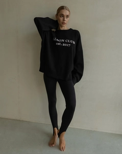 Detail of black oversized knit sweater featuring white Alson Club letter print on front
