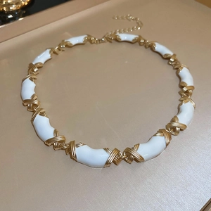 Détail de maillons en X dorés avec segments en émail blanc sur un collier vintage