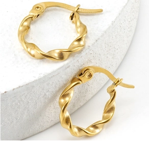 Macro detail of gold-plated stainless steel twisted hoop earring on stone texture