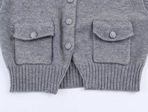 Détail du gilet en maille grise avec poches boutonnées et ourlet côtelé sur blanc