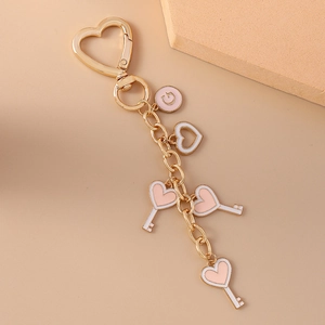 Detail of a gold cat keychain featuring pink heart charms and a letter G round pendant
