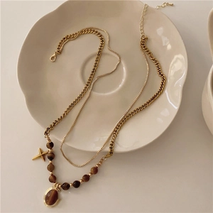 Detail of double-layer gold necklace featuring tiger eye stone and cross pendant