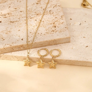 Vintage gold star pendant necklace and earrings set displayed on natural travertine stone