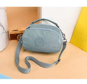 Close-up of grey-blue multi-zipper crossbody bag with adjustable strap and top handle