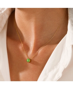Detail of a minimalist gold chain necklace with a green round gemstone on a model