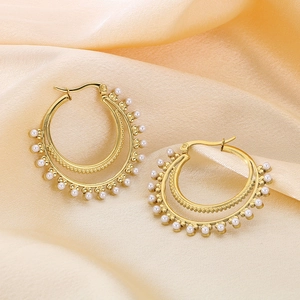 Macro detail of double-layer gold hoop earrings with white pearl accents on silk fabric