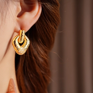 Detail of gold textured diamond earrings shown on ear with elegant twisted metal pattern