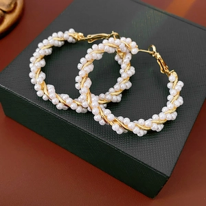 Close-up of pearl intertwined gold hoop earrings displayed on a black jewelry box