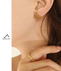 Detail of golden stainless steel butterfly stud earrings and rectangle gemstone ring on model