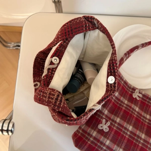 Detail view of red plaid tote bag interior with magnetic closure and bow embroidery