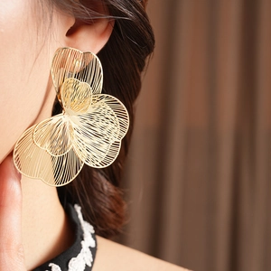 Gros plan d'une grande boucle d'oreille fleur évidée en or portée par un mannequin