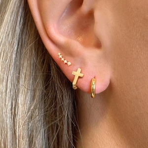 Close-up of minimalist gold cross earrings and curved stud with five inlaid diamonds