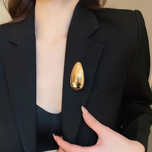 Polished gold teardrop brooch pinned on a black suit jacket for a luxury aesthetic