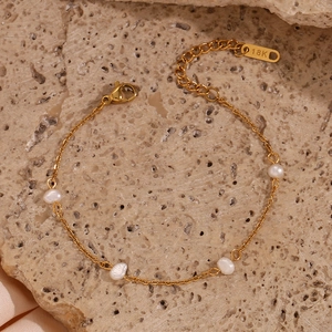 Macro detail of gold-plated chain bracelet with freshwater pearls on a stone base