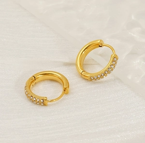 Close-up of golden hoop earrings with pavé set diamonds on a clean textured background