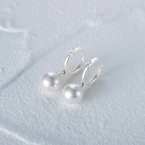 Detail of s925 silver pearl earring with zircon stones on a gray stone surface