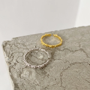 Detail of gold and silver S925 rings with irregular bubble texture on a stone surface