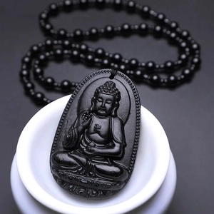 Macro detail of obsidian Buddha amulet featuring intricate Sakyamuni carvings and black beads