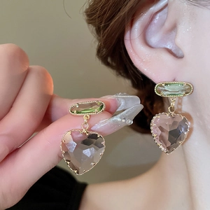 Detail of heart-shaped crystal earrings with green emerald-cut stones in gold setting