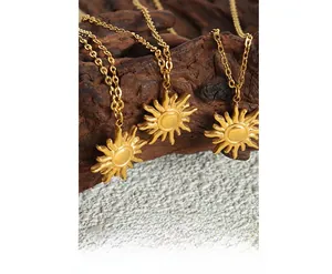 Close-up of three 18K gold-plated sun pendants on a cross chain over rustic wood
