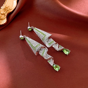 Detailed macro view of silver geometric spiral earrings with green teardrop pendants