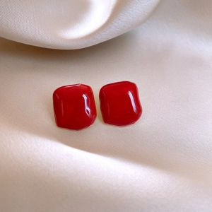 Macro shot of glossy red square earrings on soft beige silk fabric background
