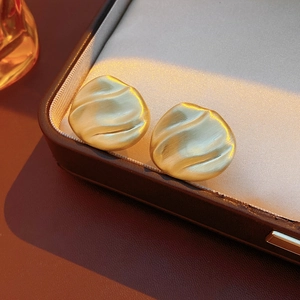 Macro shot of matte gold irregular stud earrings with wavy brushed texture on leather