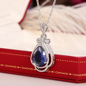 Elegant pear cut blue sapphire pendant necklace with bow design on a red jewelry box