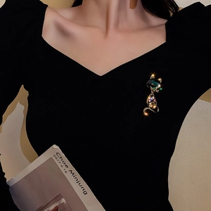 Detail of elegant gold cat brooch with green rhinestone on black V-neck clothing