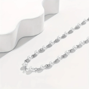 Detail view of silver metal chain with white pearls and cross pendant for men