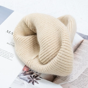 Detailed view of the beige rabbit fur knit beanie showing thick ribbed texture on a magazine