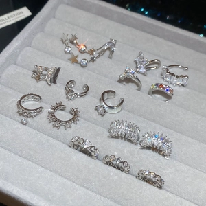 Macro shot of silver zircon ear cuffs and rings on a gray velvet jewelry display case