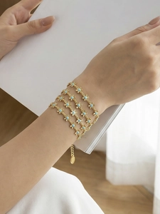 Close-up of gold wrap bracelet with small blue enamel flowers on a female wrist
