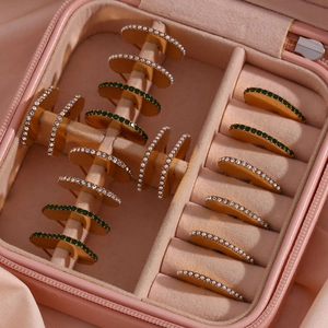 Detail of gold-plated geometric earrings with green gemstones and white pearls in a box