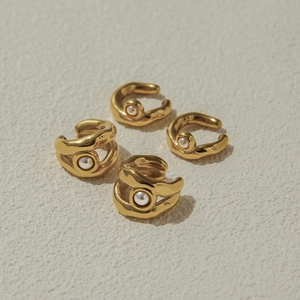 Dettaglio di quattro ear cuff dorati con perle eleganti su una superficie beige opaca