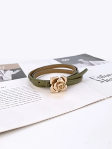 Detail of army green slim leather belt with a golden 3D rose buckle on a magazine background