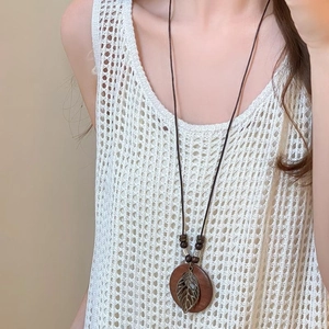 Detail of vintage wooden pendant necklace with metal leaf on white knitted sweater